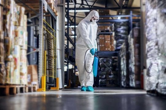 Man in protective suit and mask disinfecting warehouse